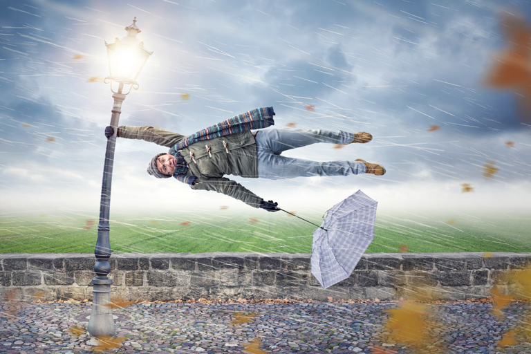 Woman holding onto lamp post as the wind blows her away